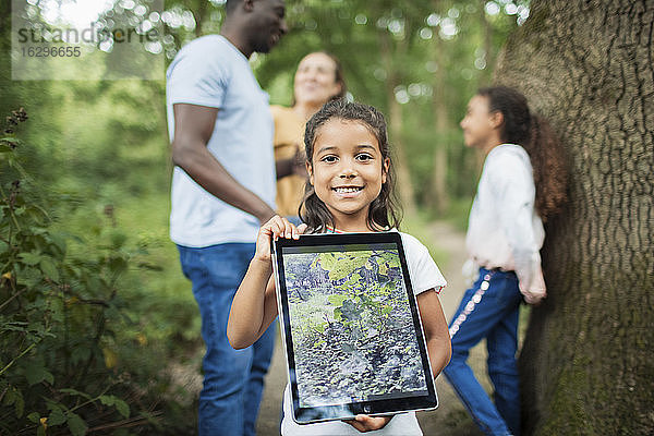 Portraitmädchen hält digitales Tablett mit Foto einer Pflanze im Wald