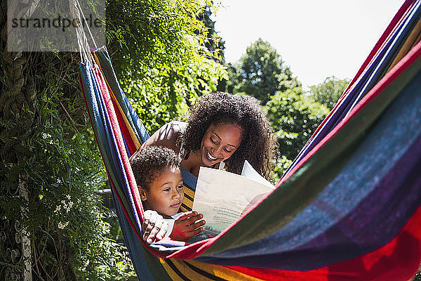 Mutter und Sohn lesen Buch in sonniger Sommerhängematte im Garten