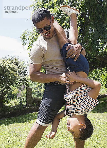 Verspielter Vater hält Sohn im sonnigen Sommerhinterhof auf dem Kopf
