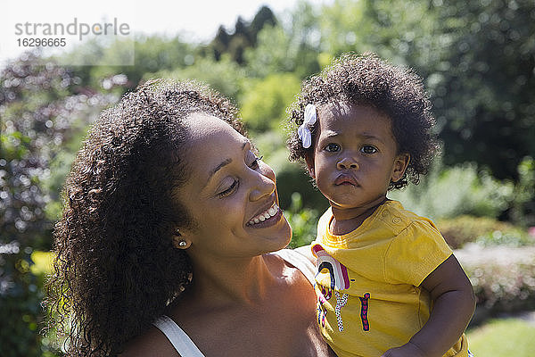 Porträt einer glücklichen Mutter  die ein süßes Kleinkind in einem sonnigen Hof hält