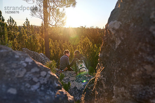 Liebenswertes junges Wandererpaar entspannt sich auf Felsen in sonnigen Wäldern bei Sonnenuntergang