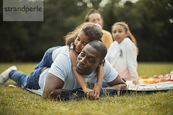 Liebevolle Tochter umarmt Vater auf Picknickdecke im Park