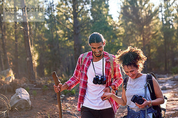 Glückliches junges Paar wandert mit Fernglas und Kamera in sonnigen Wäldern