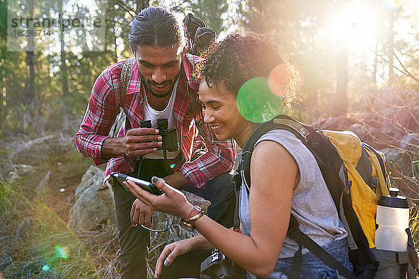 Glückliches junges Wanderpaar mit Smartphone in sonnigen Wäldern