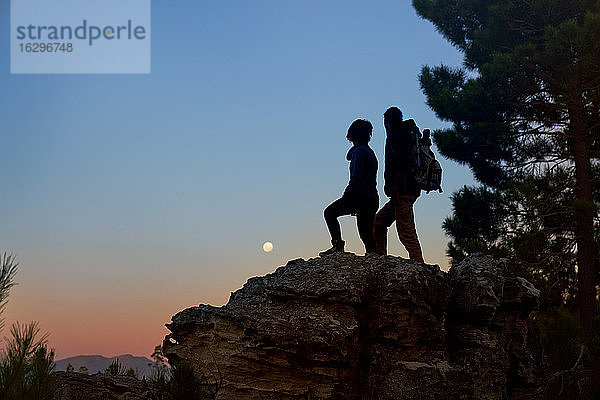 Junges Wandererpaar geniesst in der Dämmerung den Blick vom Felsen auf den Mond