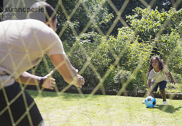 Vater und Tochter spielen Fussball im sonnigen Sommerhinterhof