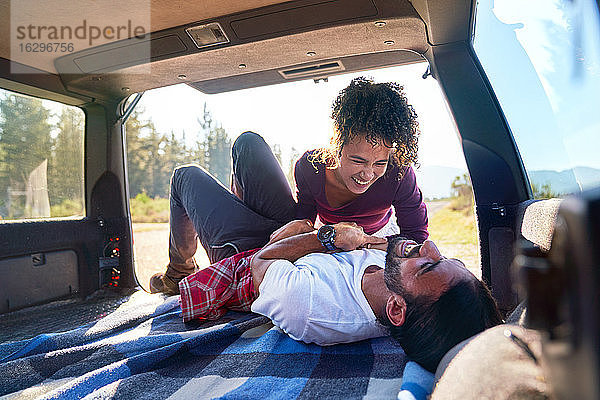 Glückliches  verspieltes junges Paar lacht auf einer Autofahrt hinten im Auto