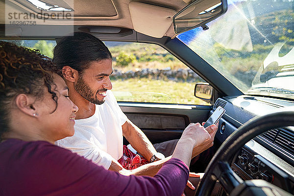 Junges Paar nutzt Smartphone auf Autoreise im sonnigen Auto