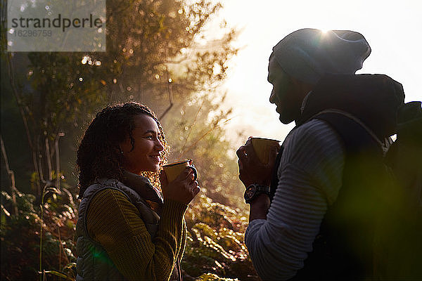 Glückliches junges Wanderpaar trinkt Kaffee in sonnigen Wäldern