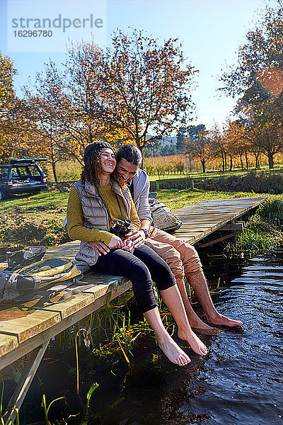 Liebenswertes barfüßiges junges Paar lacht auf dem sonnigen Dock