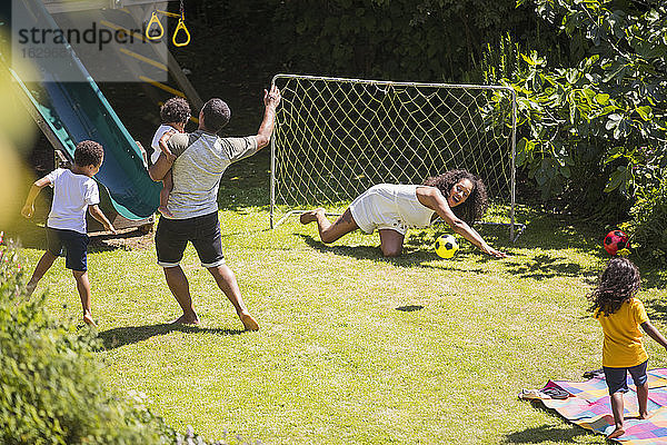 Glückliche Familie spielt Fussball im sonnigen Sommerhinterhof