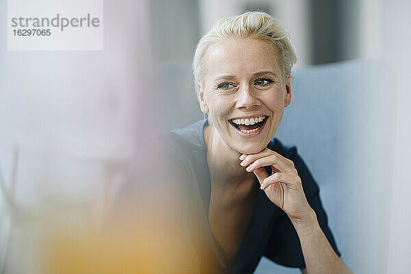Nahaufnahme einer Geschäftsfrau mit Hand am Kinn  die lachend im Büro sitzt