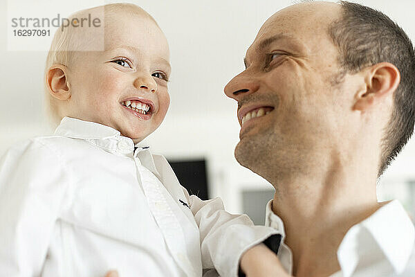 Vater lächelt  während er einen kleinen Jungen ansieht  während er zu Hause steht