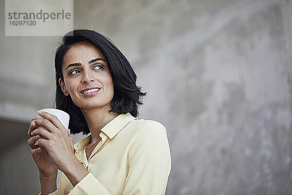 Nahaufnahme einer nachdenklichen Geschäftsfrau  die eine Kaffeetasse an die Wand eines Büros hält