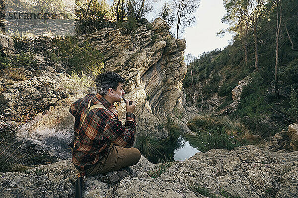 Buschmann raucht Pfeife  während er auf einer Felsformation sitzt