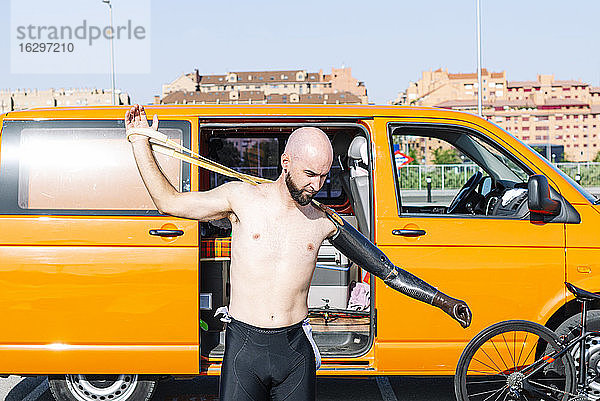 Kahlköpfiger Anpassungssportler  der eine Handprothese trägt  während er gegen einen Lieferwagen steht