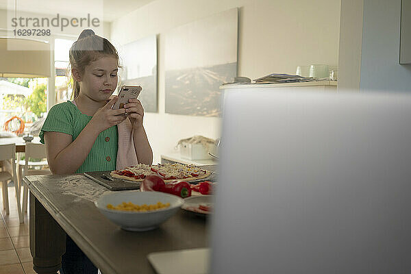 Mädchen  das eine Pizza über einer Kücheninsel fotografiert