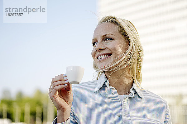 Lächelnde blonde Frau  die eine Kaffeetasse hält und in den Himmel schaut
