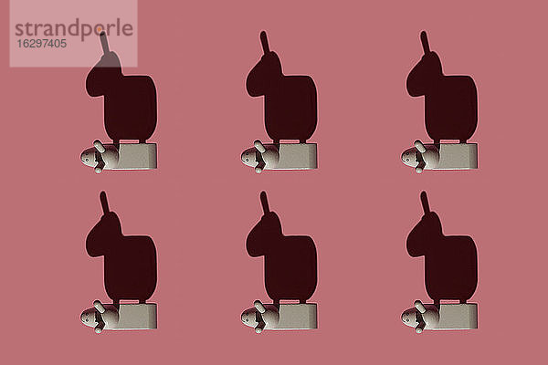 Muster aus kleinen braunen Eselfiguren vor pastellrotem Hintergrund