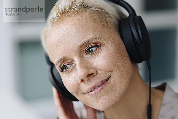 Nahaufnahme einer nachdenklichen Geschäftsfrau  die im Büro über Kopfhörer Musik hört