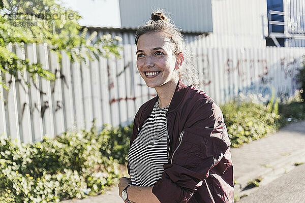 Lächelnde junge Frau  die wegschaut  während sie an einem sonnigen Tag auf der Straße steht