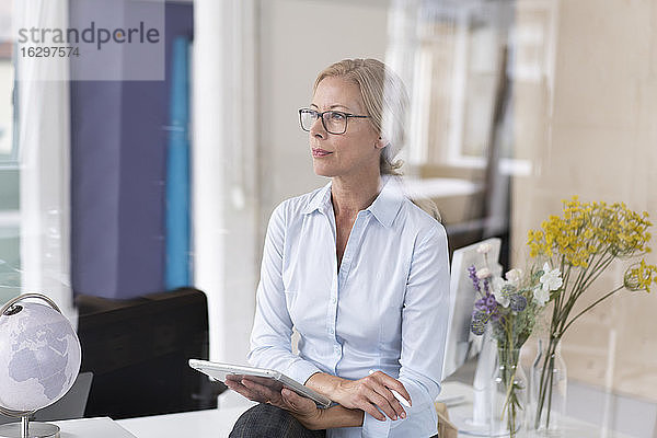 Nachdenkliche Geschäftsfrau mit digitalem Tablet im Home Office sitzend