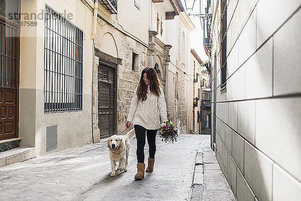 Frau hält Blumenstrauß beim Spaziergang mit Hund auf der Straße in der Stadt