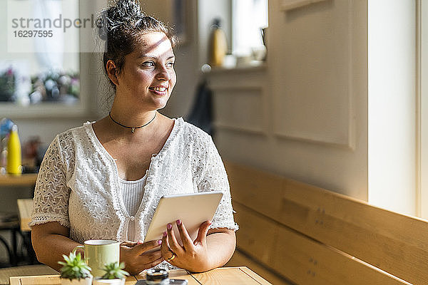Nachdenkliche junge Frau mit digitalem Tablet  die an einem Tisch in einem Café sitzt