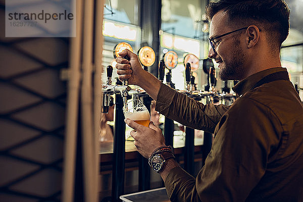 Lächelnder Barkeeper zapft Bier in einer Kneipe