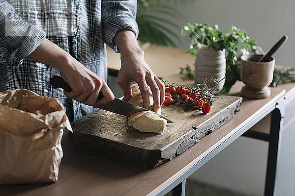 Hände eines Mannes  der frisches  hausgemachtes Brot auf einem Brett in der Küche schneidet
