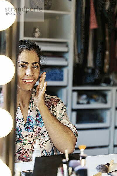 Reflexion einer jungen Frau im Spiegel  während sie ihre morgendliche Schönheitsroutine zu Hause durchführt