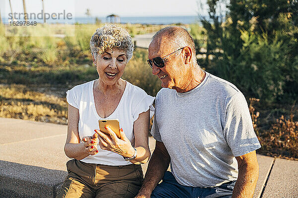 Älterer Mann und Frau telefonieren im Park sitzend