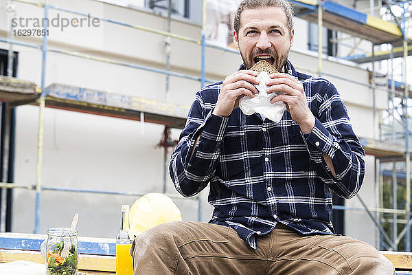 Bauarbeiter isst Brot  während er auf der Baustelle an einem Gebäude sitzt