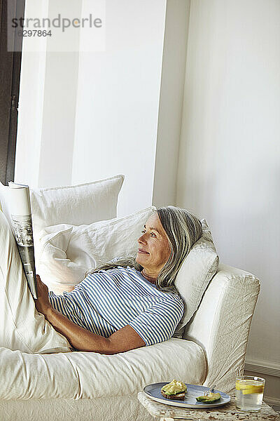 Frau liest Zeitschrift auf Sofa im Wohnzimmer