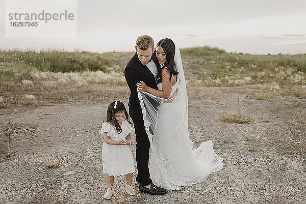Eltern mit Tochter im Hochzeitskleid stehen gegen den Himmel