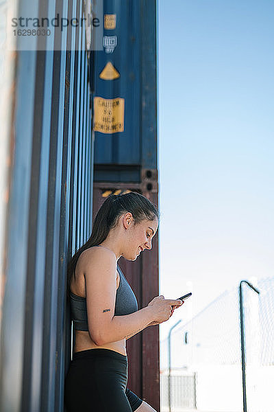 Sportliche Frau benutzt Smartphone im Industriegebiet