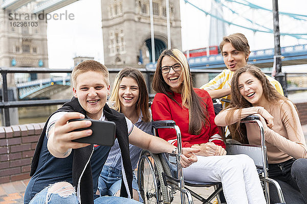Glückliche junge männliche und weibliche Freunde machen ein Selfie mit der Tower Bridge im Hintergrund  London  UK
