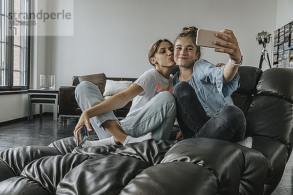 Freunde machen ein Selfie mit ihrem Smartphone  während sie zu Hause auf der Couch sitzen