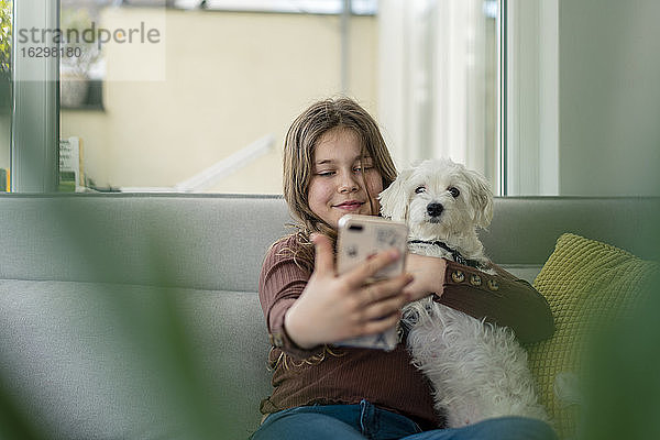 Mädchen nimmt Selfie durch Smartphone mit Hund auf Sofa