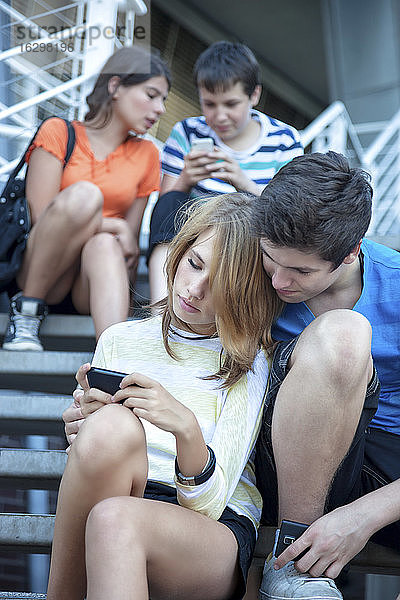Freunde im Teenageralter benutzen mobile Geräte auf Treppen