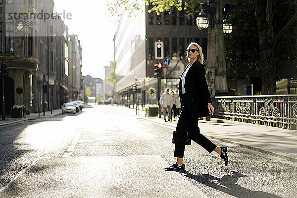 Modische Geschäftsfrau beim Überqueren der Straße in der Stadt
