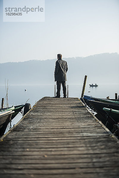 Mann steht auf einer Holzpromenade und schaut auf den See
