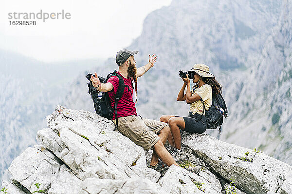 Junge Frau  die einen Mann fotografiert  während sie auf einem Berggipfel an der Ruta Del Cares sitzt  Asturien  Spanien