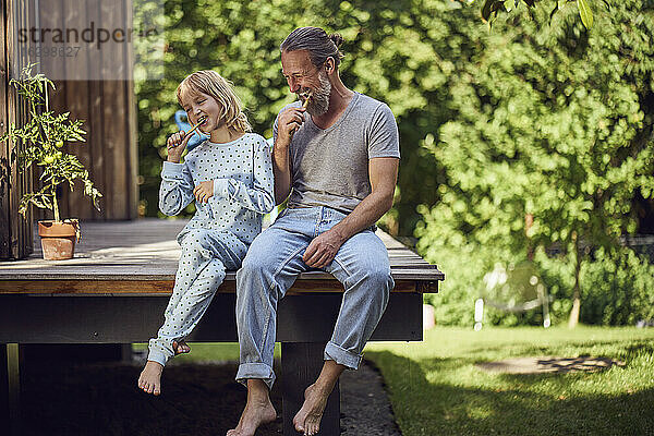 Vater und Tochter beim Zähneputzen im Garten sitzend