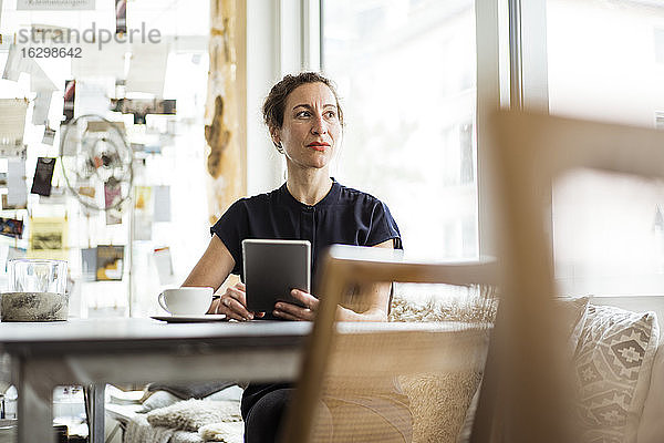 Nachdenkliche Besitzerin mit Kaffee auf dem Tisch und digitalem Tablet in einem Restaurant