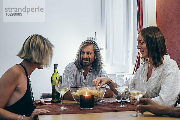 Lächelnde junge Freunde  die bei einem geselligen Beisammensein am Tisch Wein trinken