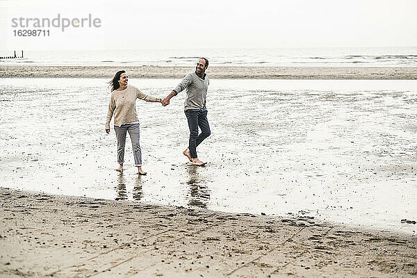 Paar hält Hände beim Spaziergang am Strand gegen den Himmel