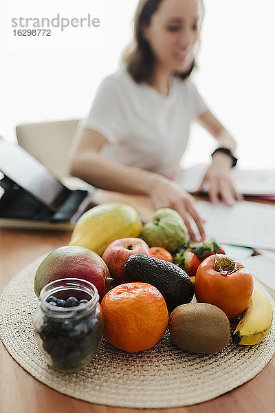 Obst auf dem Tisch mit einer Frau  die im Hintergrund zu Hause arbeitet
