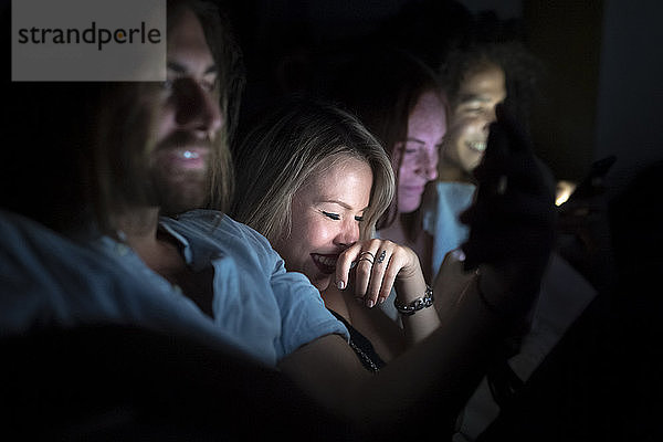 Lächelnde Freunde  die nachts ihr Smartphone benutzen