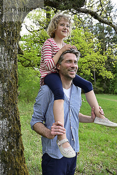 Lächelnder Vater  der seine Tochter auf der Schulter trägt  während er den Wald erkundet